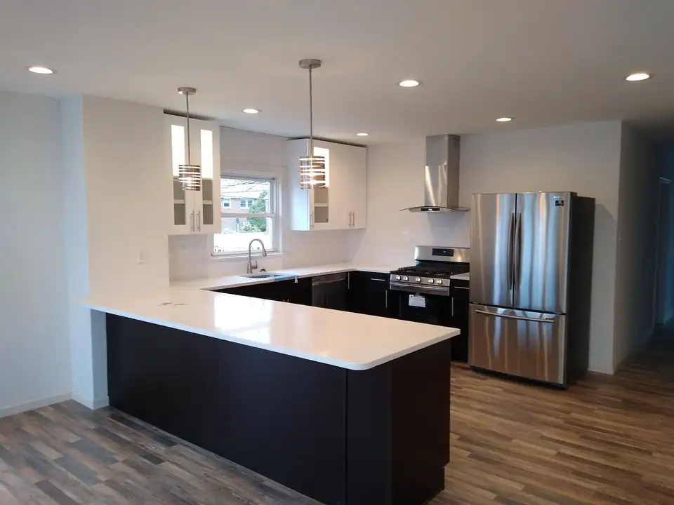 Kitchen remodeling in Philadelphia: white upper cabinets, dark peninsula with white quartz top, stainless appliances and pendant lights